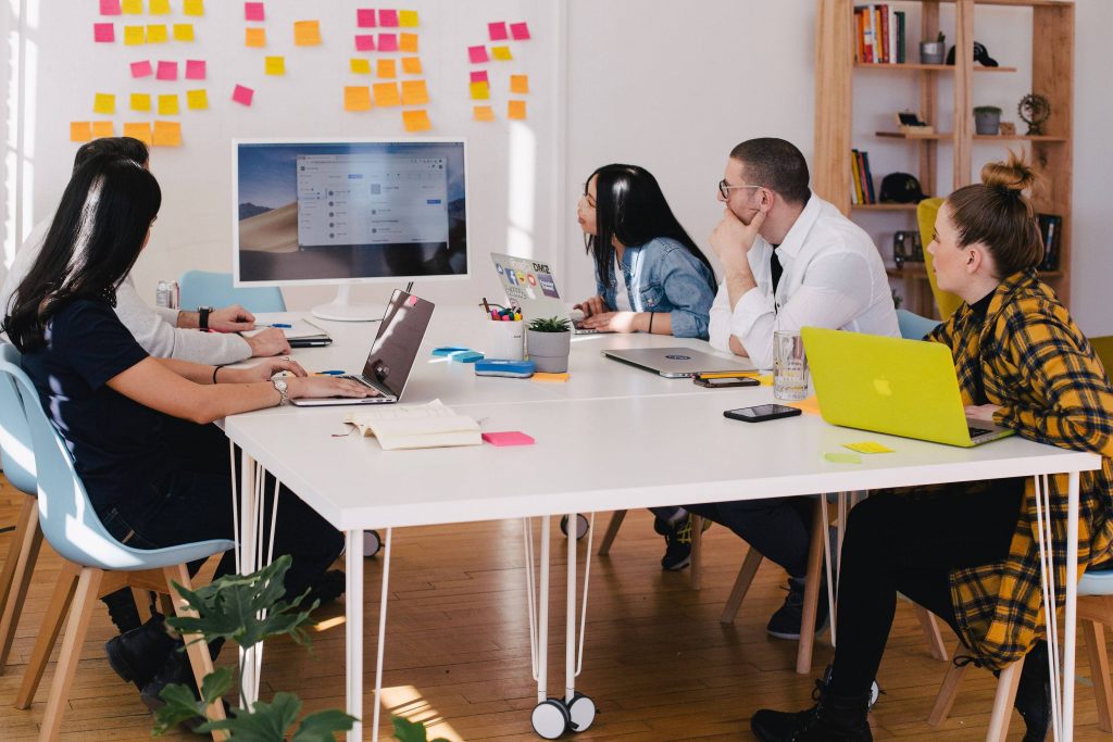 People in a brainstorming meeting with a computer screen and a notice board with Post-Its